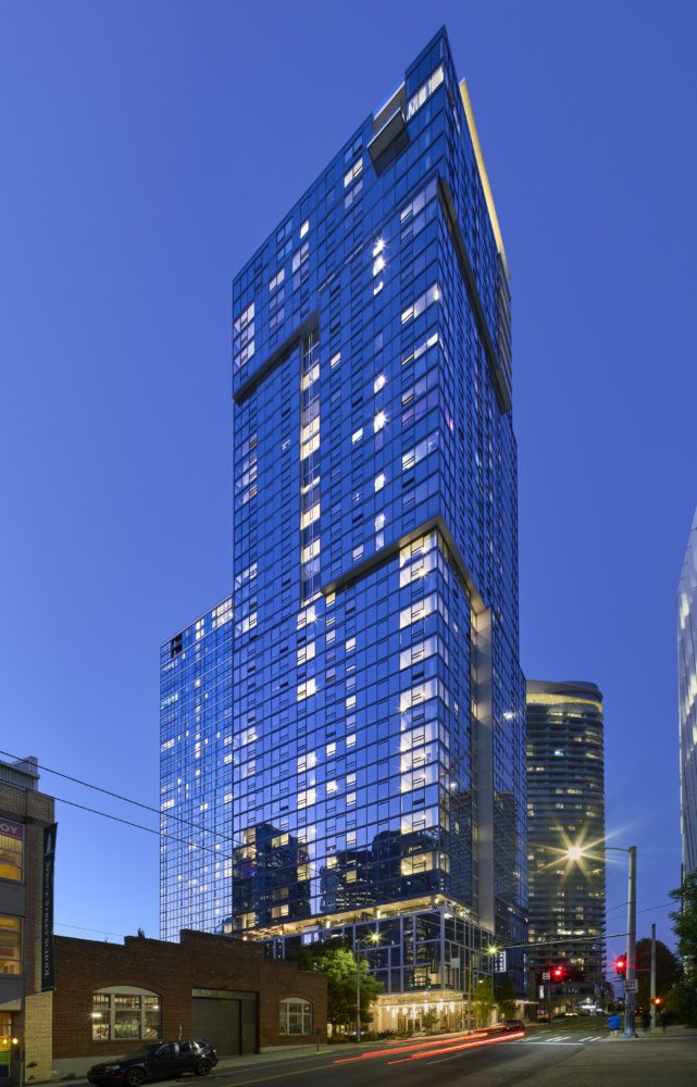 full building photo of the ayer at nighttime with the city lights in downtown seattle