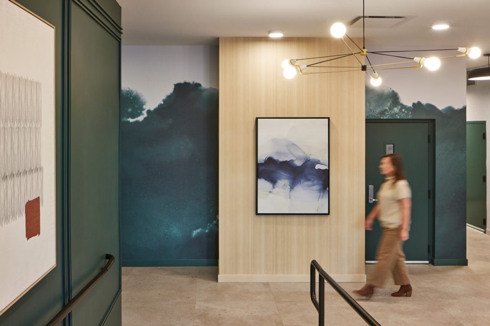 photo of a woman walking in front of a blue mural and painting design detail that mimics the puget sound with sophisticated lighting above